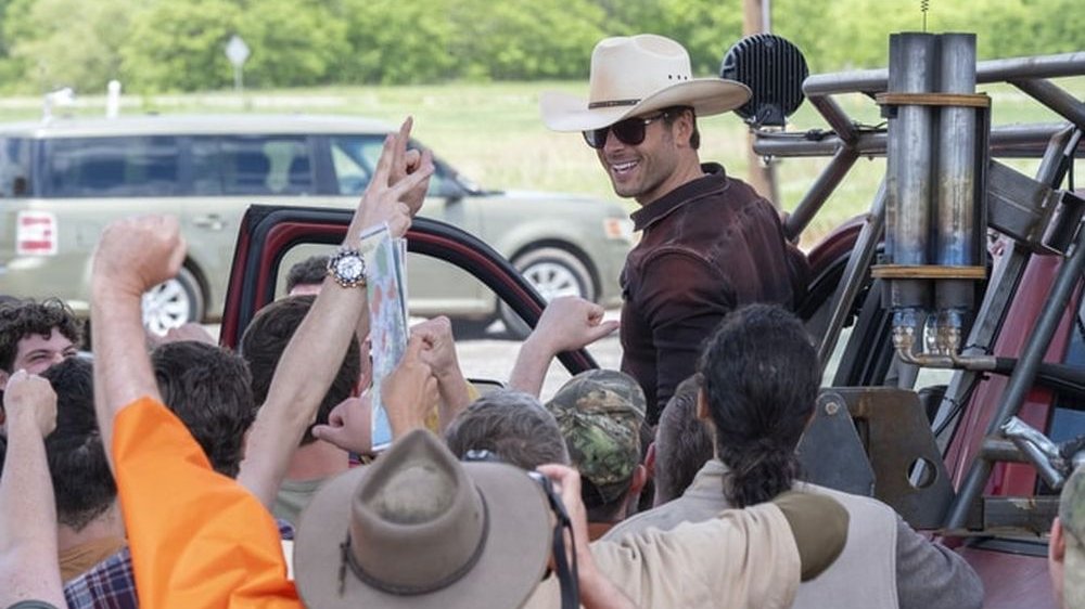 Mężczyzna w kowbojskim kapeluszu uśmiecha się do grupy swoich fanów.