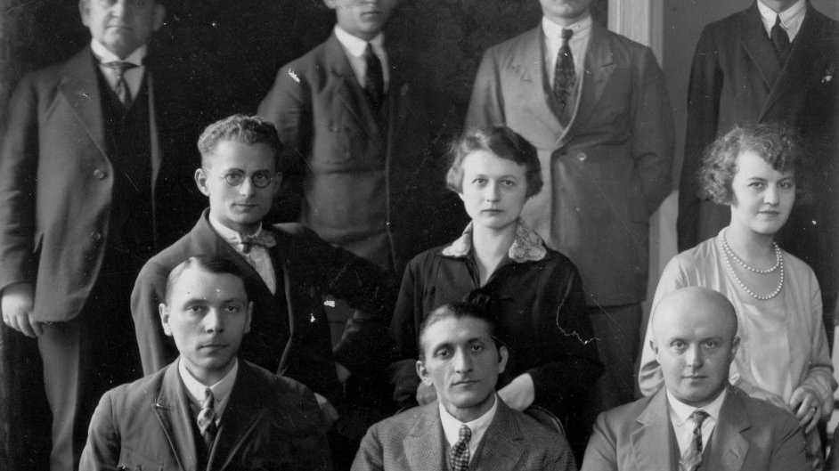 Czarno-białe zdjęcie grupowe elegencko ubranych kobiet i mężczyzn. Część grupy stoi, część siedzi.