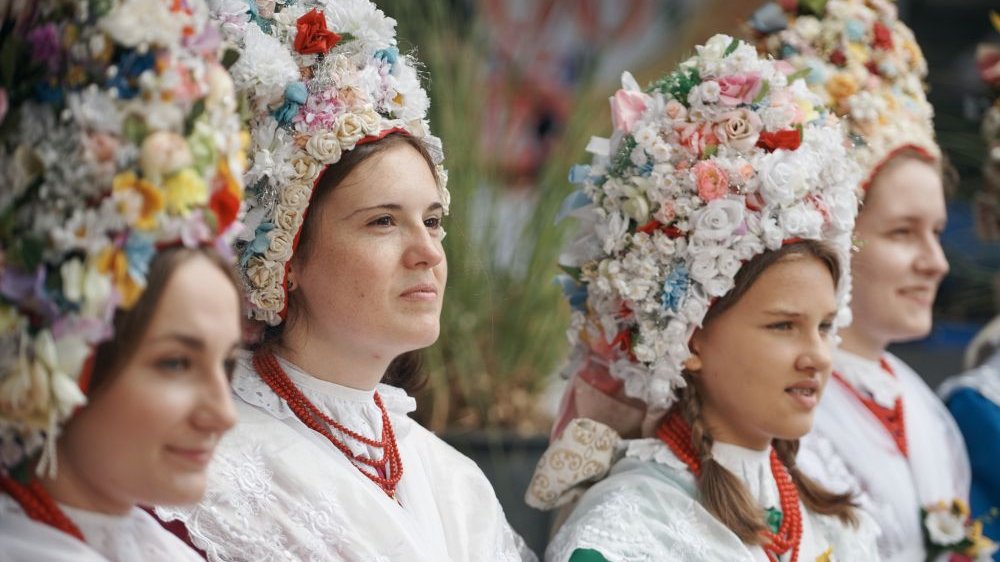 Młode kobiety w tradycyjnych strojach bamberskich, z kolorowymi karnetami z kwiatów na głowach.