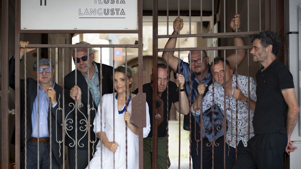 Sześciu mężczyzn i jedna kobieta pozują do zdjęcia zza starej bramy z białą tabliczką "Tłusta langusta".