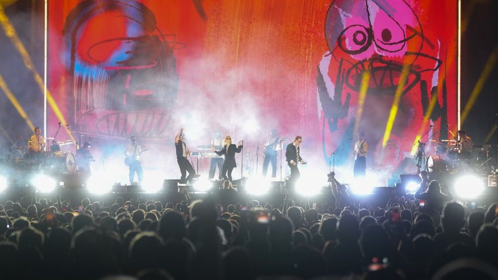 Koncert na plenerowej scenie. Jest już ciemno, za artystami wyświetlają się ogromne, kolorowe wizualizacje.