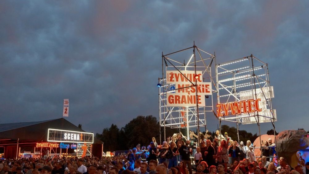 Ludzie na festiwalu. Dookoła nich neony sponsora imprezy i jej nazwa oraz mniejsza scena.