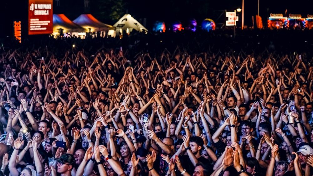 Tłum ludzi pod sceną klaszcze unosząc ręce w górę. Jest już ciemno, oświetla ich tylko światło padające ze sceny.