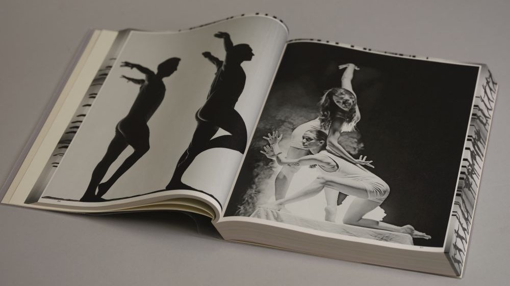 Rozkładówka książki. Po lewej zdjęcie dwóch nagich męskich sylwetek, po prawej dwie kobiety w tańcu na scenie.