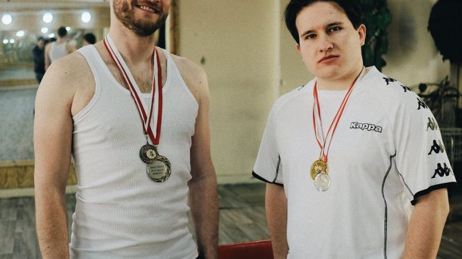 Dwóch mężczyzn w białych koszulkach pozuje z medalami na szyi.