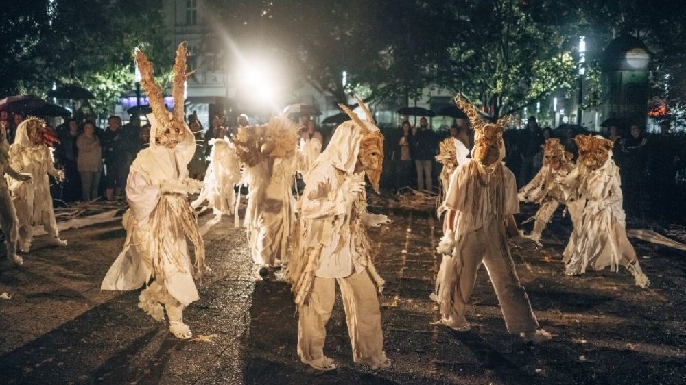 Kilkanaście postaci ubranych w białe, powyciągane i lekko poszarpane szaty, mają na głowach maski upodabniające do różnych zwierząt - uszy zająca, rogi kozła, maskę misia czy bociana.