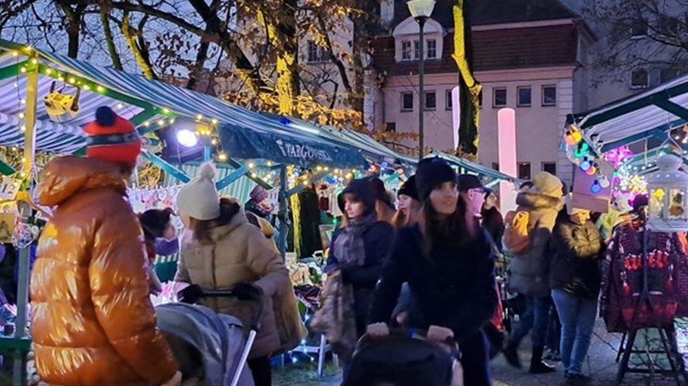 Tłum ludzi przechadza się między straganami. Jest prawdopodobnie popołudnie, bo robi się już ciemno.