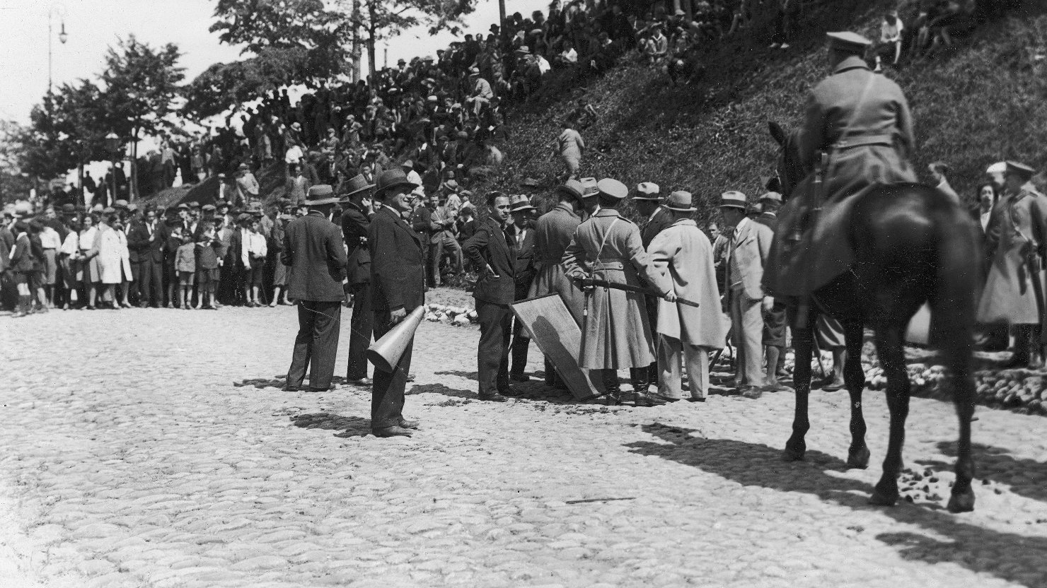 Zdjęcie archiwalne. Scena z realizacji filmu. Tłum aktorów i obserwujących na wale. W centrum mężczyzna w kapeluszu z megafonem.