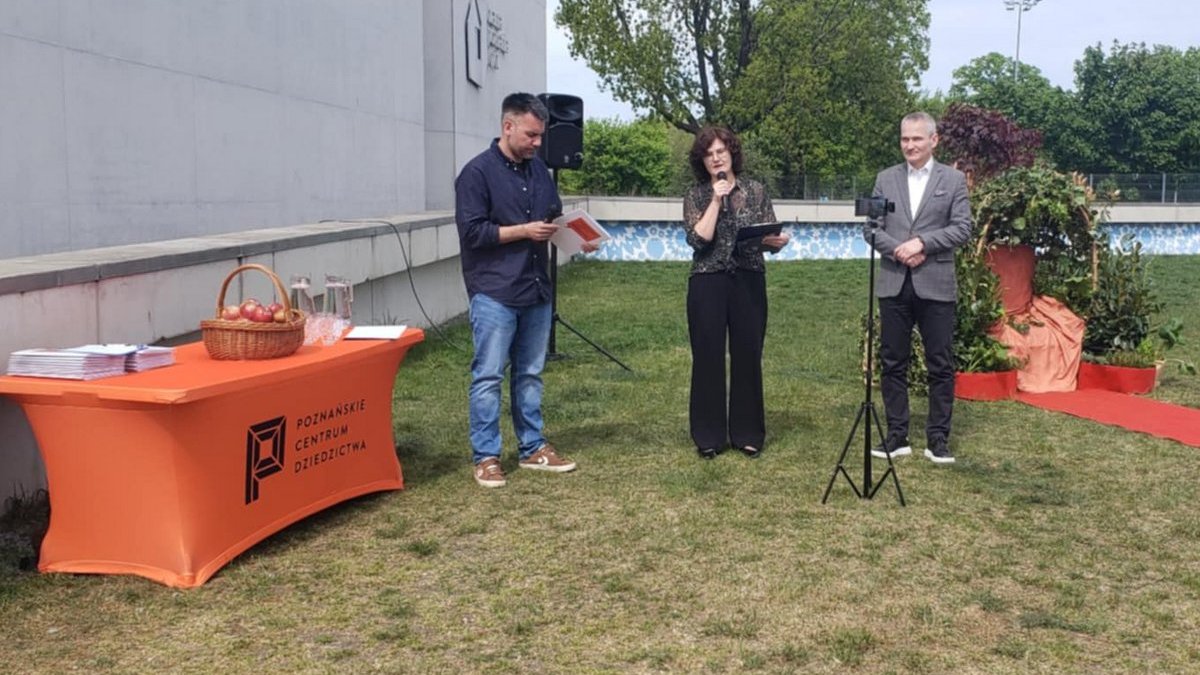 Trzy osoby, dwóch mężczyzn i kobieta, stojące na trawniku omawiają plan wydarzeń