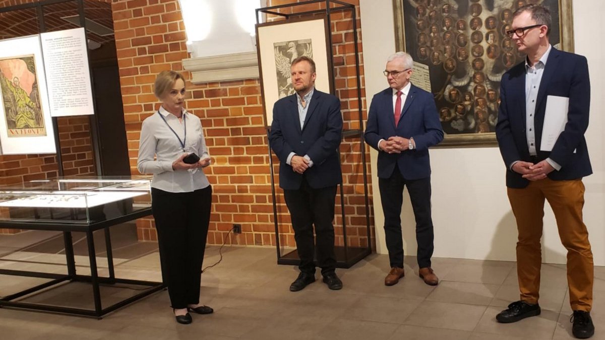 Mężczyźni i kobieta w sali wystawienniczej muzeum, za nimi obraz, obok eksponaty