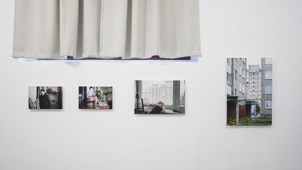 Biała firanka, biała ściana, a na niej kolorowe fotografie bez ramek.