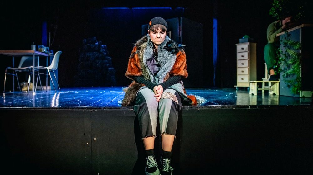 Smutna dziewczyna siedzi na skraju sceny patrząc w dół.