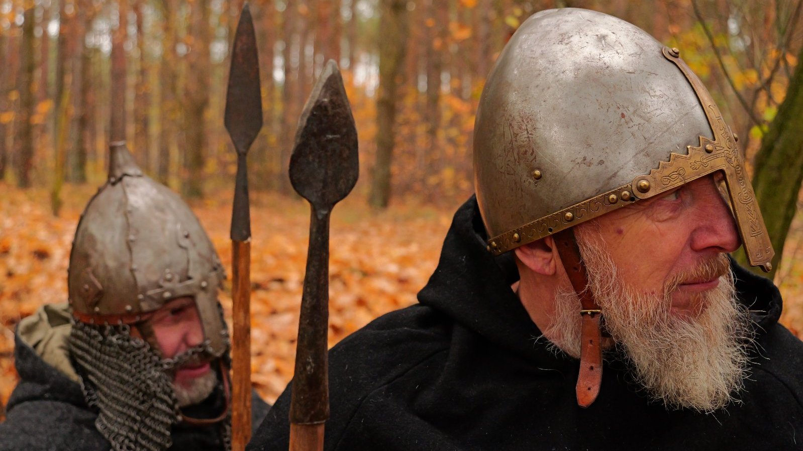 Dwóch wojów w metalowych hełmach, z włoczniaki, czai się w lesie