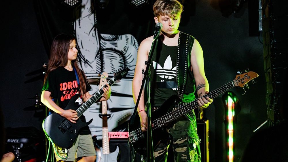 Dwóch nastolatków na scenie gra na gitarach.