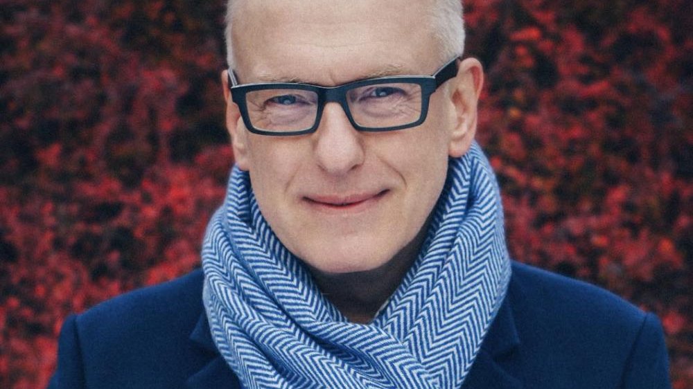 Uśmiechnięty mężczyzna w szaliku na tle czerwonego, jesiennego bluszczu.