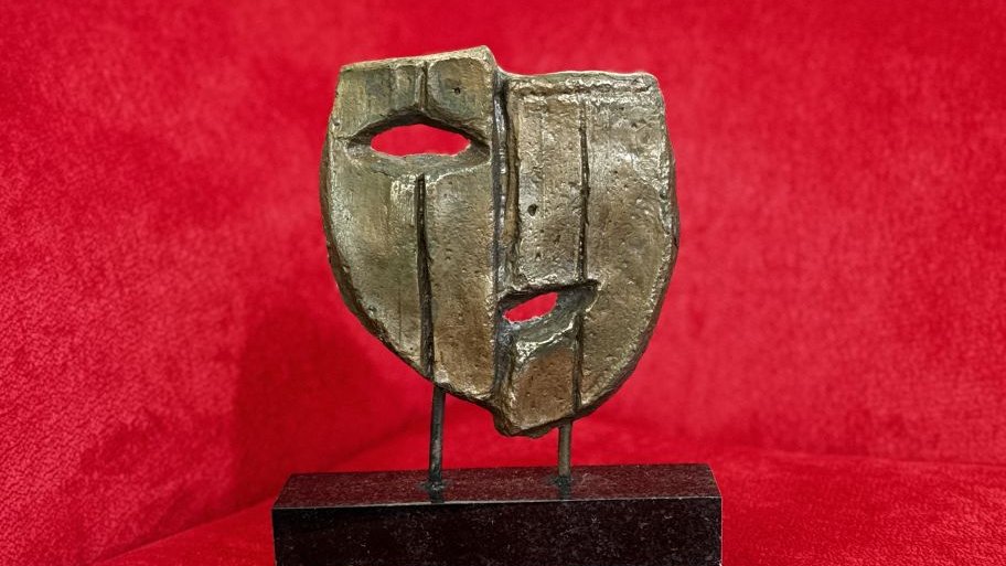Statuetka na dwóch nóżkach, przedstawiająca maskę teatralną z okiem i ustami