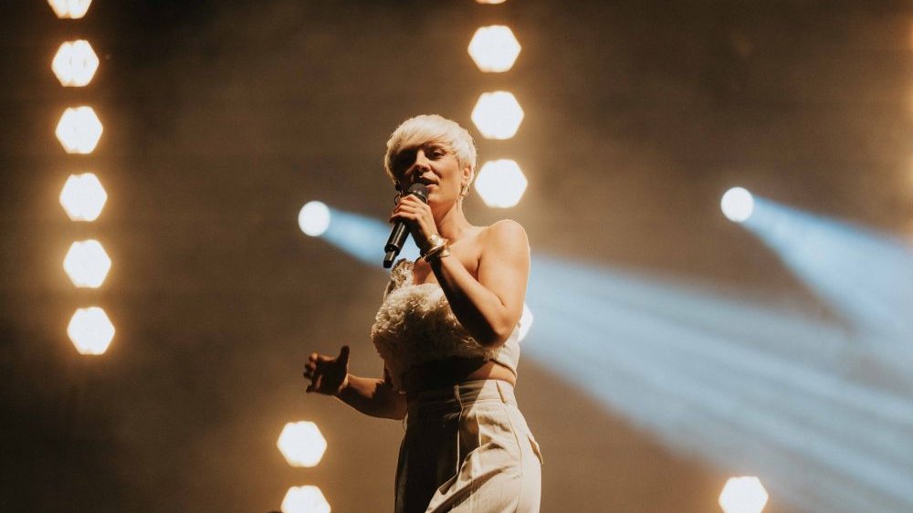Wokalistka w krótkiej blond fryzurze śpiewa na scenie.