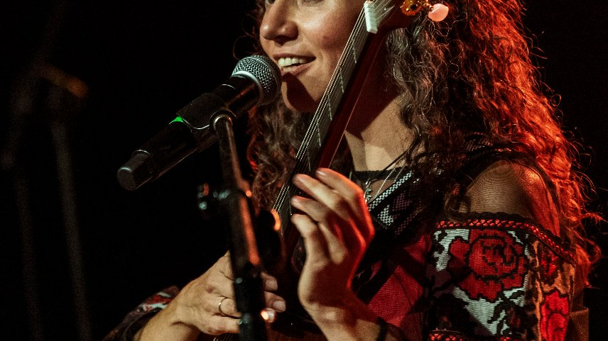 Młoda kobieta w rozpuszczonych, kręconwych włosach gra ba gitarze.