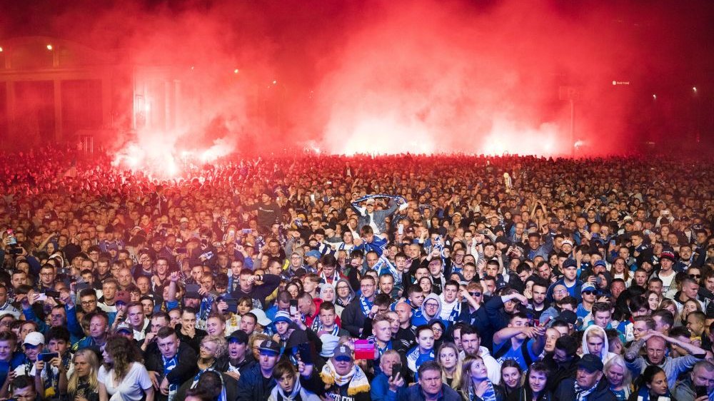 Tłum kibiców Lecha Poznań w biało-niebieskich szalikach.