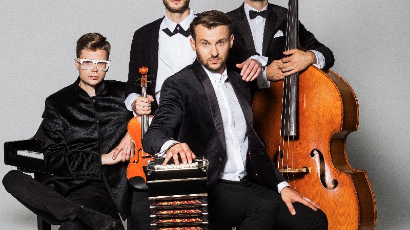 Czworo wystrojonych muzyków z instrumentami. Dwóch siedzi, dwóch stoi.