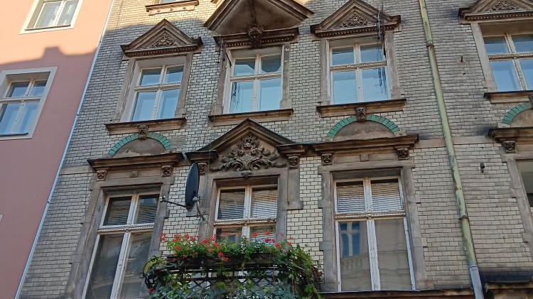 Widok na front kamienicy pokryty białą cegłą.