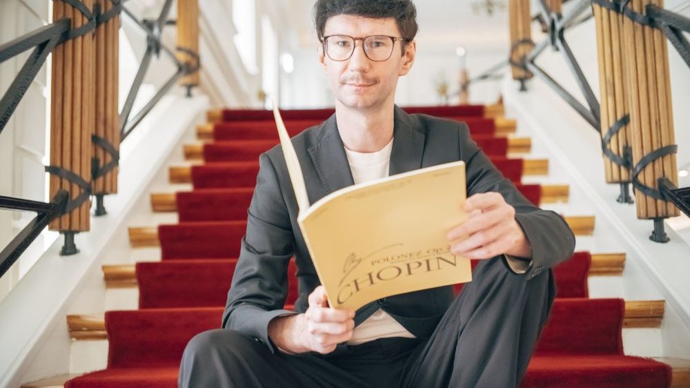 Jakub Dera siedzi na schodach biblioteki, w rękach trzyma zeszyt nut podpisany "Chopin".