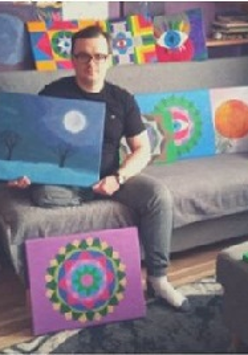 Tomasz Włodarczyk na kanapie z obrazami.