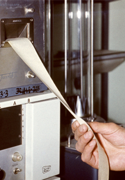 Z maszyny wychodzi taśma paieru z wydrukie. Taśmę trzyma dłoń najprawdopodobniej lekarza.