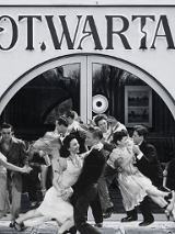 Zdjęcie przedstawia restaurację z parami oddającymi się tańcowi swingowemu. Dziewczyny w rękach swoich partnerów latają i śmieją się.