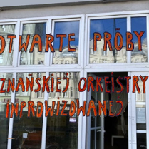 Napis na witrynie informujący o otwartych próbach Poznańskiej Orkiestry Improwizowanej.