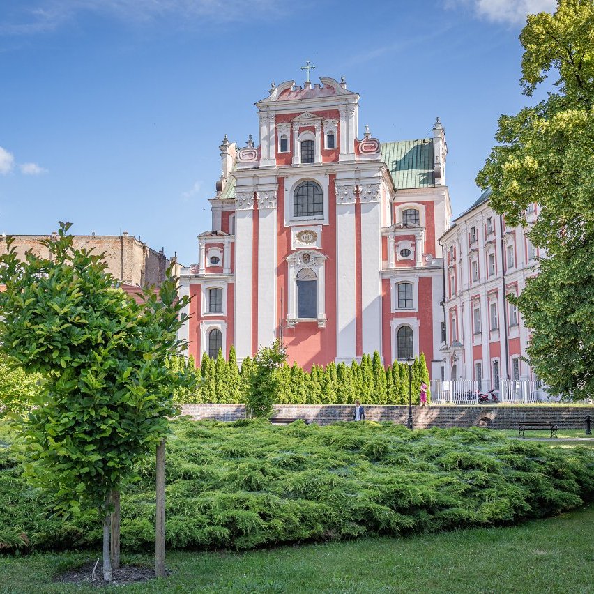 Park, trawa, drzewa, w tle biało-różowy zabytkowy budynek
