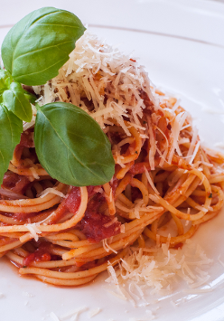 Zdjęcie makaronu z sosem pomidorowym udekorowany listkmi bazylii.