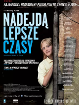 Młoda dziwczyna o blond włosach, w żółtej koszuli. Wychyla się zza wejścia do budynku.