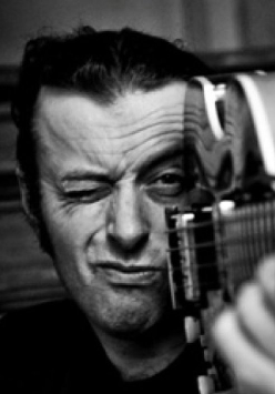 Tymon Tymański trzyma gitarę tak, jakby to była broń i celuje nią przed siebie mrużąc jedno oko