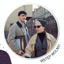 .Kobieta i mężczyzna w czapkach i płaszczach. Za nimi budynki.