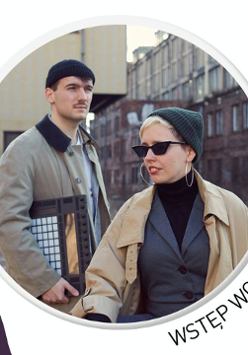 .Kobieta i mężczyzna w czapkach i płaszczach. Za nimi budynki.