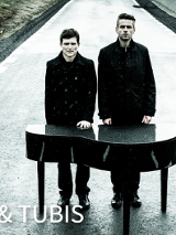 Dwóch mężczyzn ubranych na czarno, stoją na ulicy za małym fortepianem.