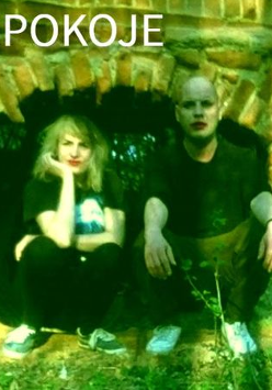 Kobieta i mężczyzna kucają przy murze. Mają pomalowane na czerwono usta.