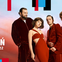 Czworo artstów (trzech męzczyzn i jedna kobieta) elegancko ubrani w odcienie czerwieni pozuja do zdjęcia na tle nieba w odcieniach czerwieni, pomarańczu i niebieskiego po zachodzie słońca.