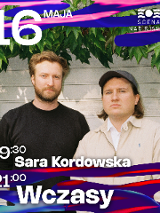 dwójka wykonawców na tle nialej sciany budynku i zwisajacych zielonych lisci