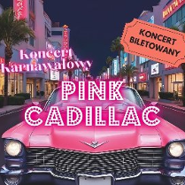 Na pierwszym planie różowy cadillac i duży biało-różowy napis "Pink Cadillac" W tle widać ulicę i budynki z oświetlonymi witrynami sklepowymi oraz palmy na chodniku.