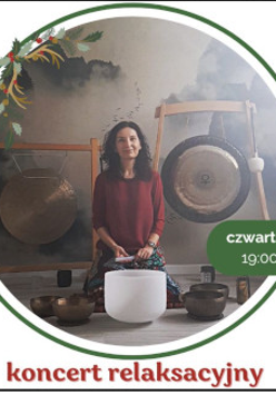 Kobieta w bordowej bluzce siedzi na podłodze. Przed nią stoją misy i gongi do grania.