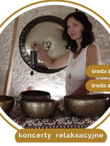 Kobieta w białej bluzce siedzi na dywanie. Przed nią stoją misy i gongi do grania.