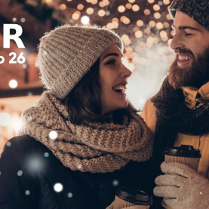 Kobieta i mężczyzna w zimowych straojach uśmiechają się do siebie, a w ręku mają kubki na gorące napoje.