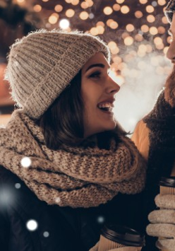 Kobieta i mężczyzna w zimowych straojach uśmiechają się do siebie, a w ręku mają kubki na gorące napoje.