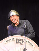 Mężczyzna w kasku śmiejący się przed mikrofonem.