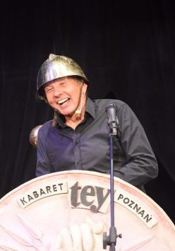 Mężczyzna w kasku śmiejący się przed mikrofonem.