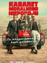 Przed maską samochodu opierając się o nią stoi dwóch mężczyzn, a za nimi na masce siedzi kolejnych dwóch.