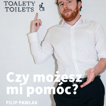 Zdjęcie mężczyzny w białej koszuli na tle białej ściany. Mężczyzna pokazuje palcem napis na ścianie.