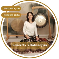 Kobieta w średnim wieku z czarnymi włosami. Ubrana w biały długi rękaw i wzorzyste spodnie. Siedzi na podłodze pokrytej dywanami. Za nią wiszą 2 gongi. Przed nią leży kilka mis.